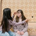 A mother lovingly adjusts her daughter's hair as they sit together on steps.