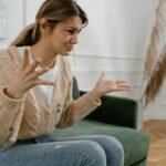 A woman sitting on a green sofa, gesturing emotionally, indoors.